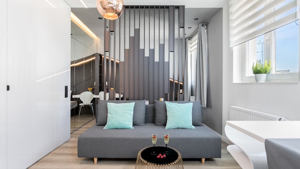Een moderne woonkamer met een grijze bank, een zwarte salontafel en een trap op de achtergrond.