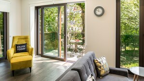 Een moderne woonkamer met een geel fauteuil, een grijze bank en een eetgedeelte zichtbaar door grote glazen schuifdeuren.