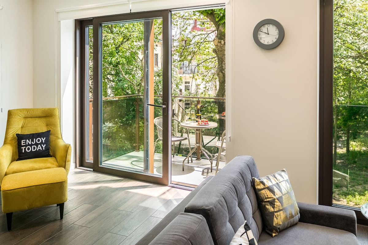 A modern living room with a yellow armchair, a grey sofa, and a dining area visible through large sliding glass doors.