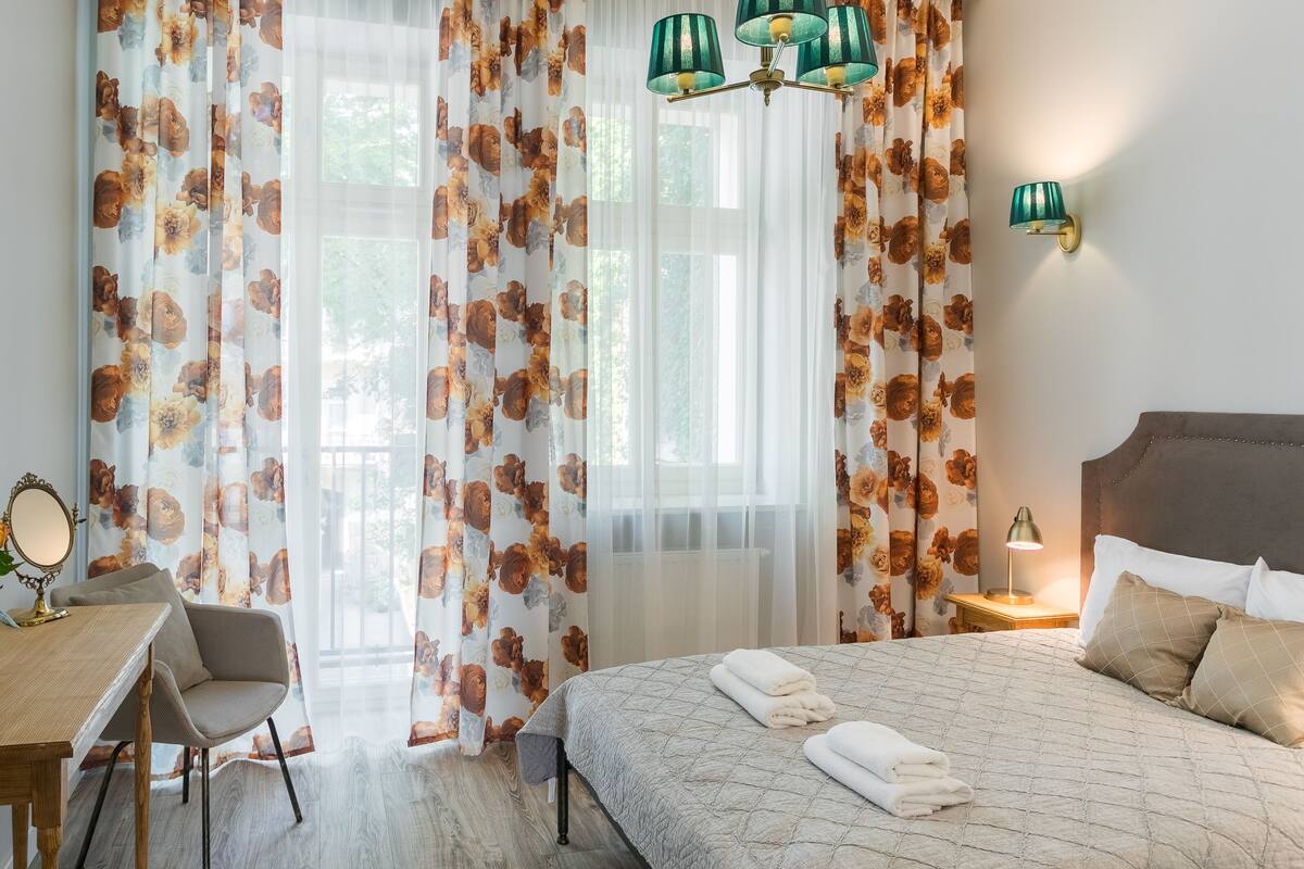 A bedroom with a bed, bedside table, chair, and a desk with a mirror.