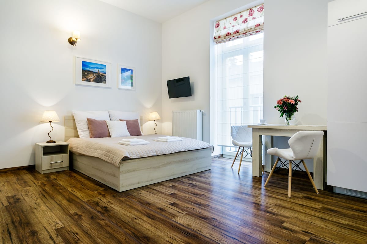 A bedroom with a bed, bedside tables, a desk with a chair, a TV, and a window with curtains.
