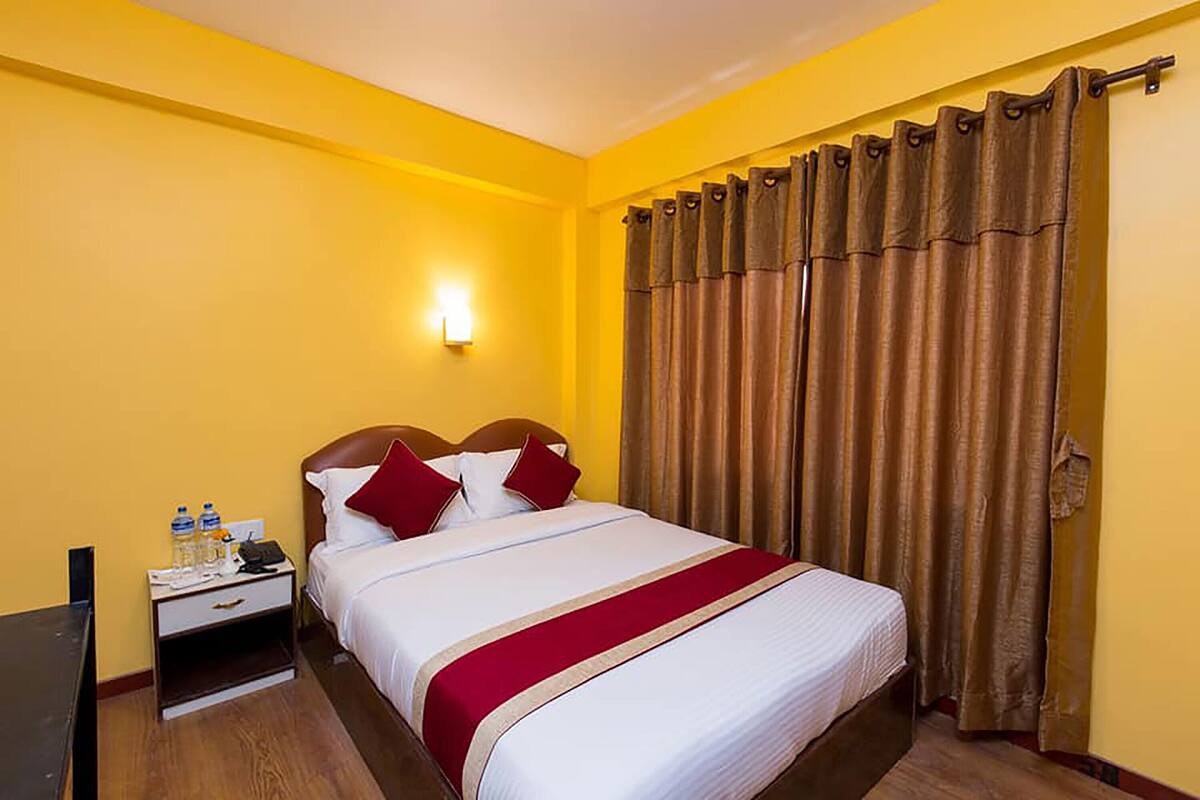 A hotel room with a bed, nightstand, and curtains.