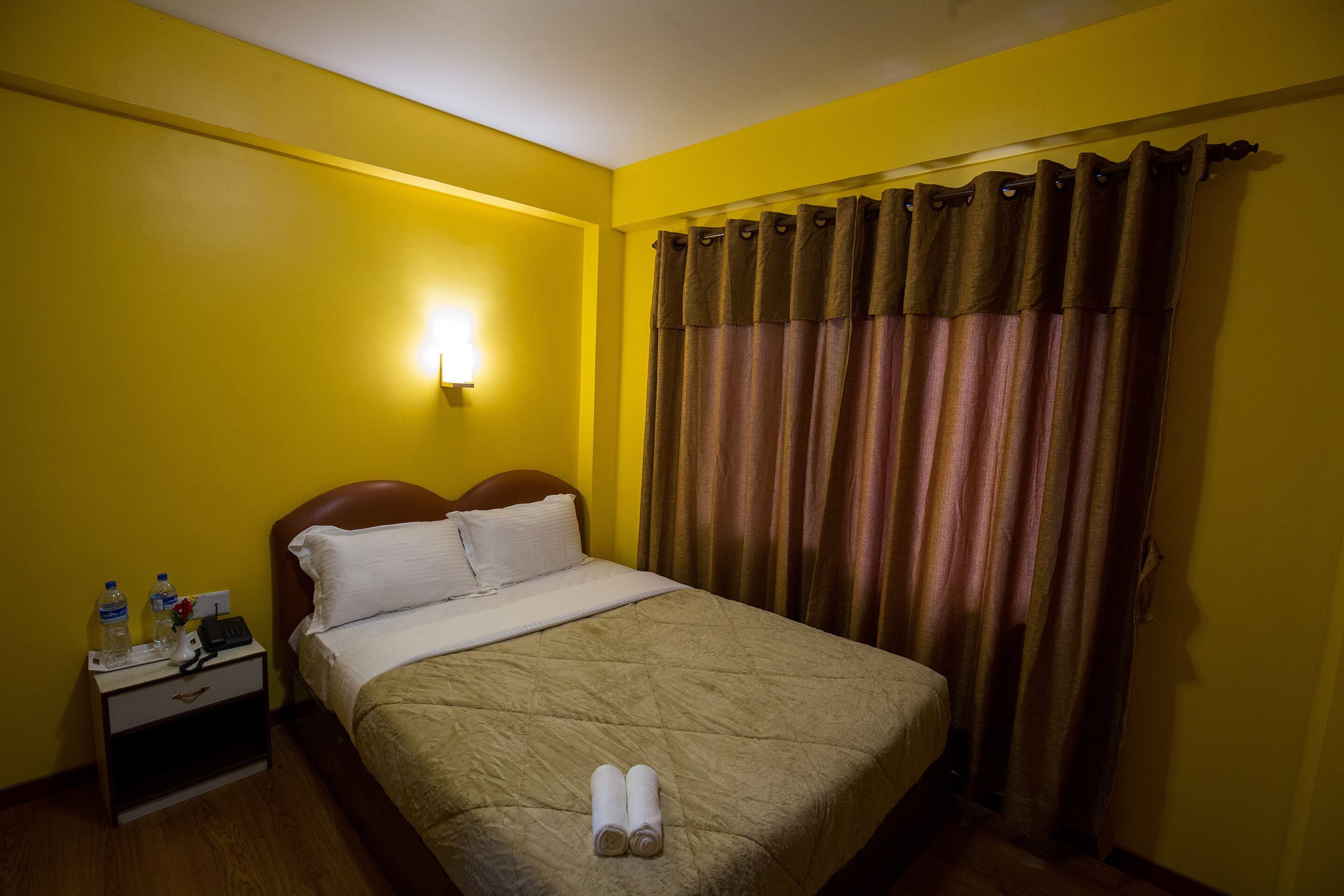 A hotel room with a bed, a nightstand with a lamp, and a curtain.