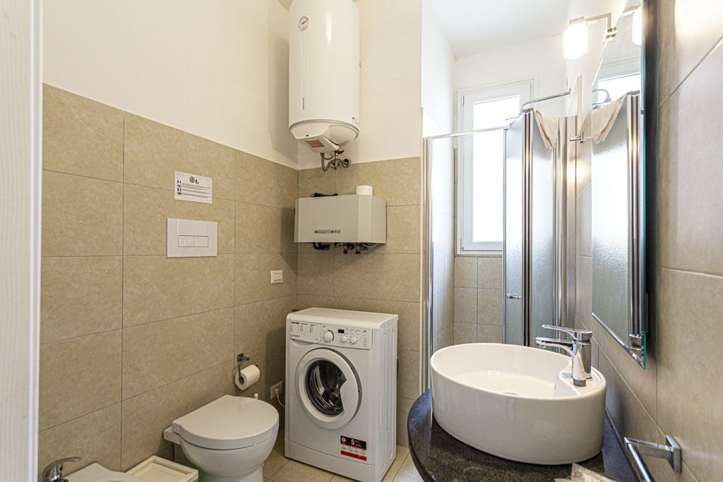 A compact bathroom with a toilet, washing machine, and sink.