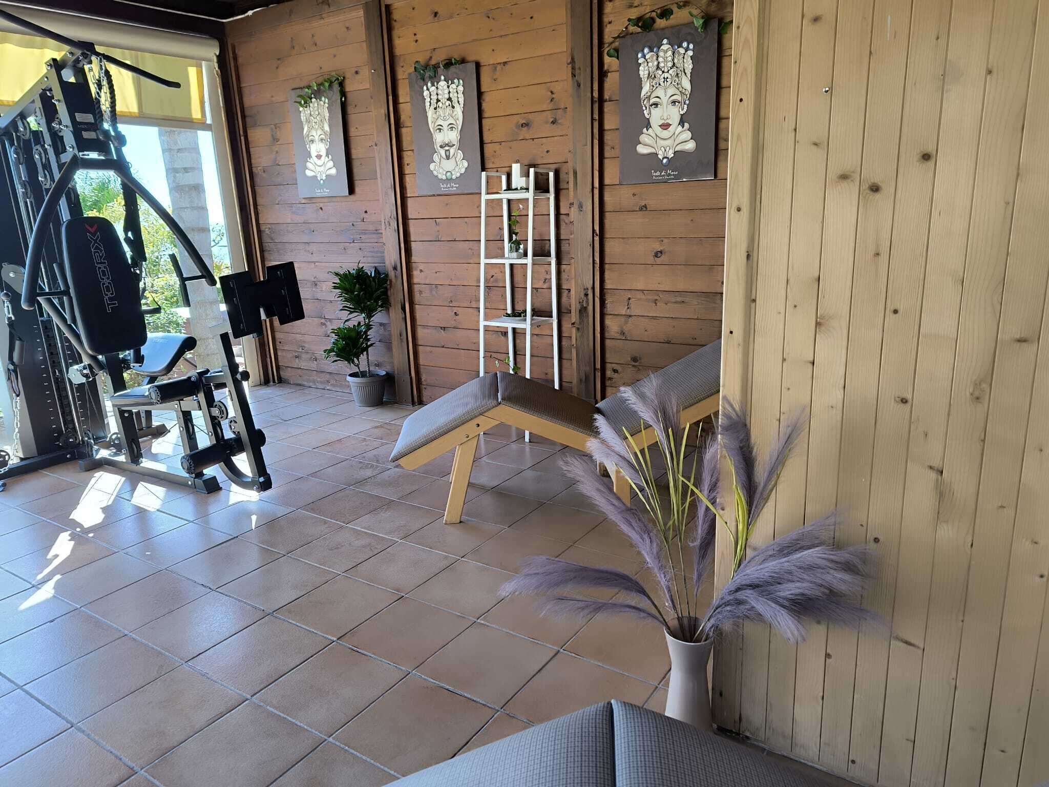 Een sportschool met trainingsapparatuur, een bank en een wandrek.