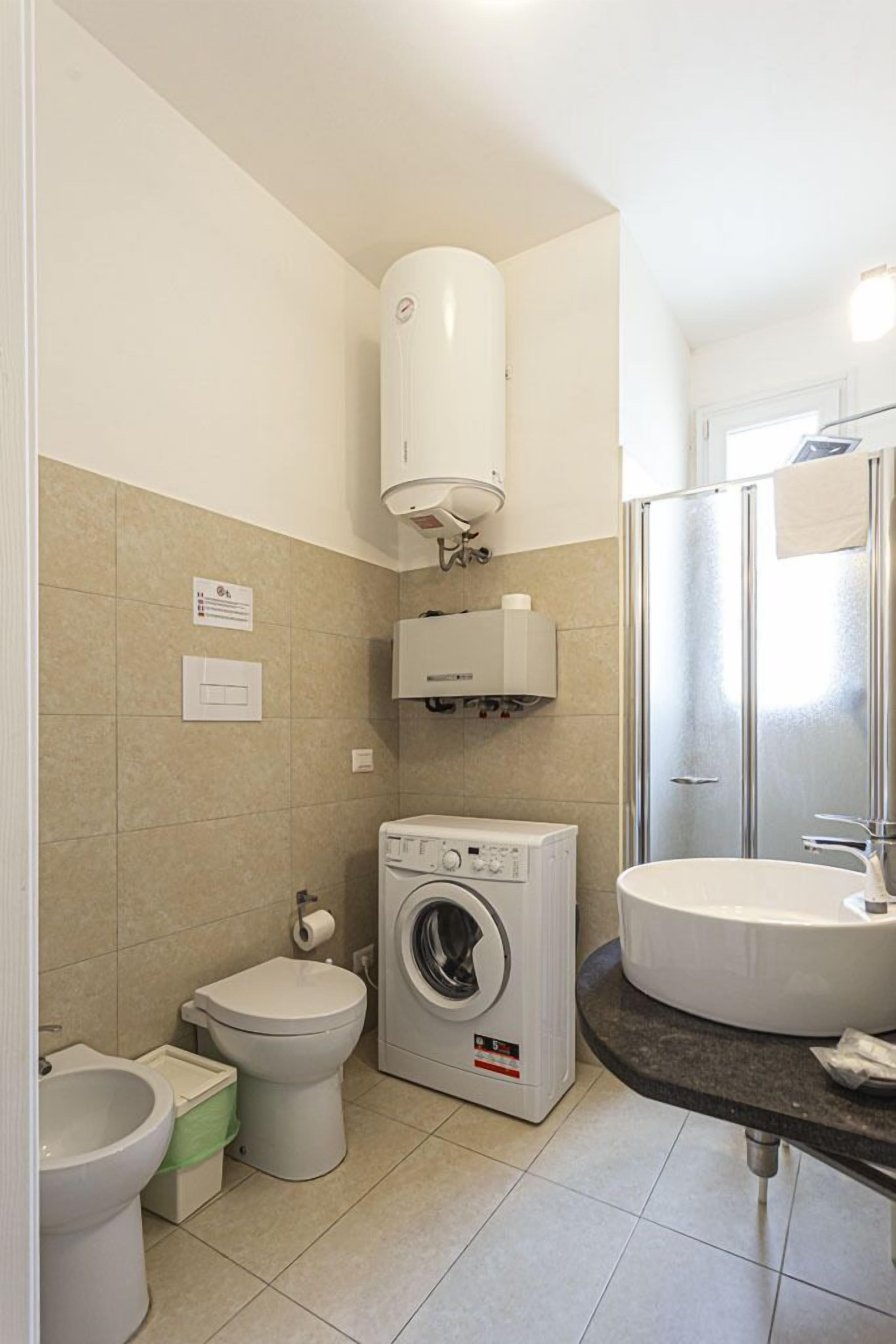 Une salle de bain compacte comprenant un lave-linge, des toilettes, un bidet et un grand lavabo.