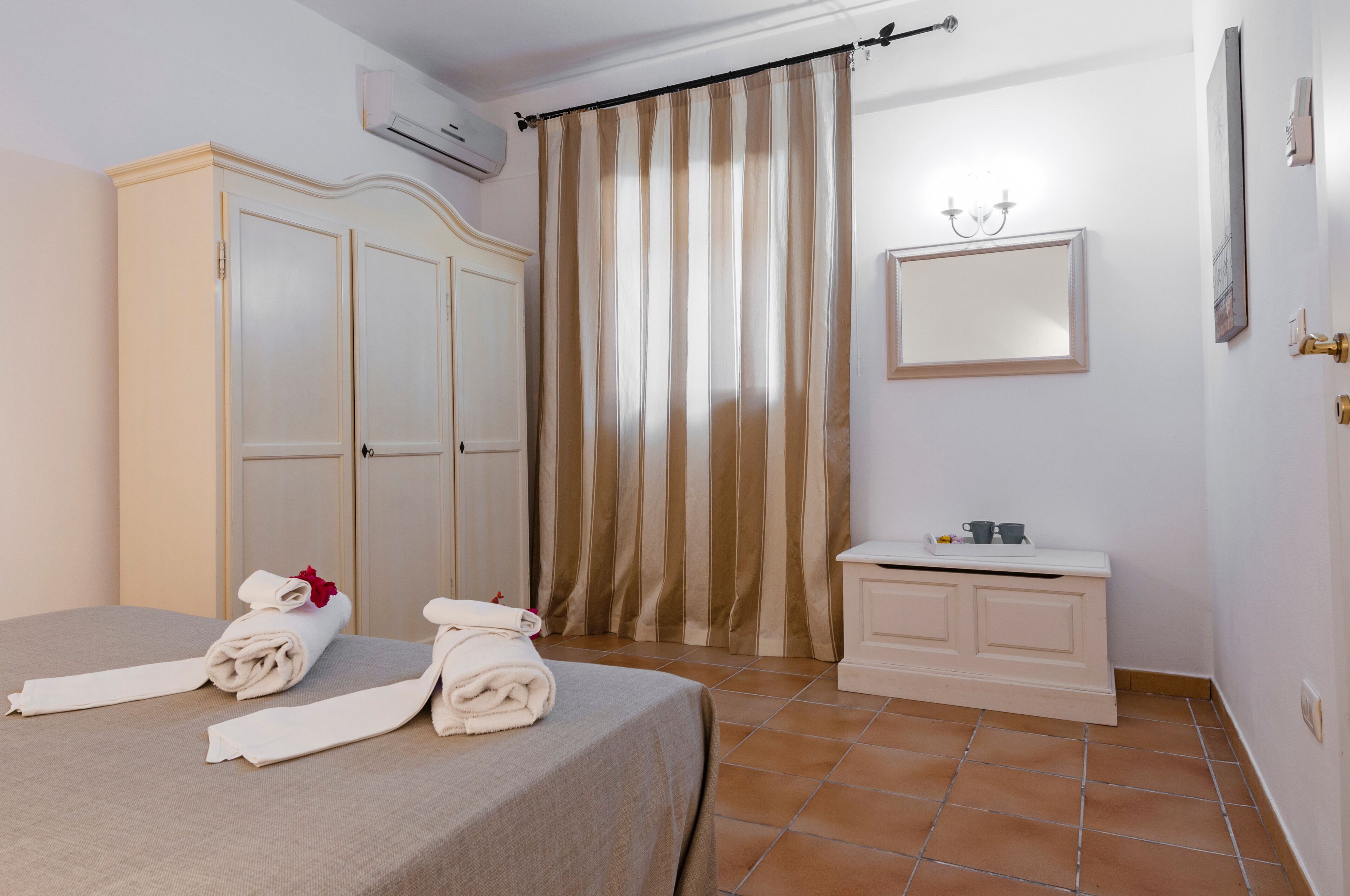 Een hotelkamer met een bed, een kledingkast, een kaptafel met spiegel en een gestreept gordijn.