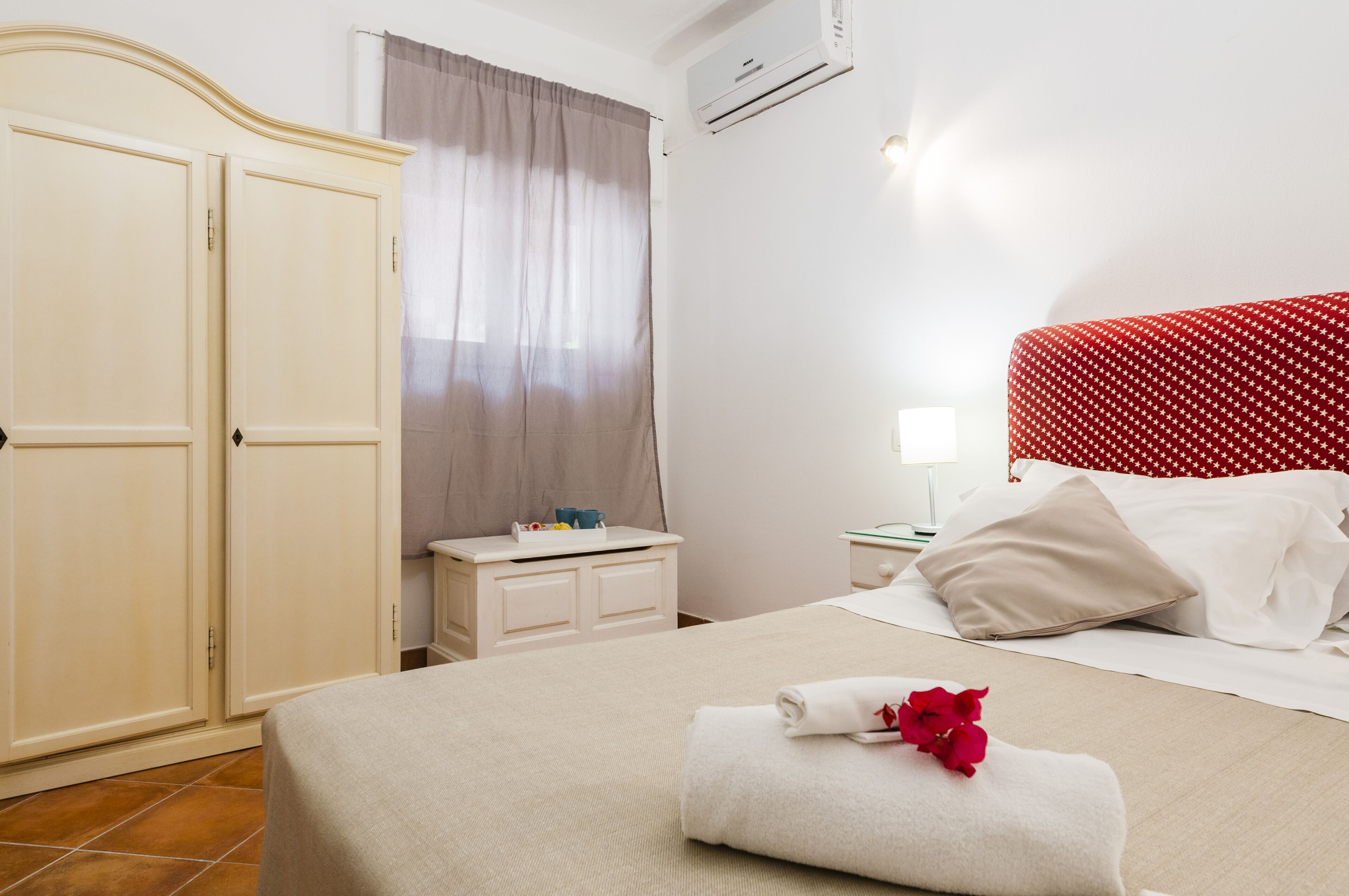 A hotel room with a bed, a wardrobe, a nightstand, and an air conditioning unit.