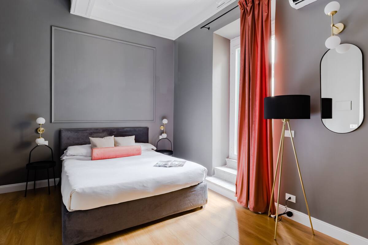 A modern bedroom with a large bed, bedside lamps, a mirror, and a window with curtains.