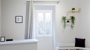 Una habitación moderna y minimalista con un banco blanco, un escritorio blanco y un ventanal con vistas a árboles.