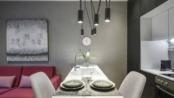 A modern dining area with a white table set for two, a red sofa, and a kitchen in the background.