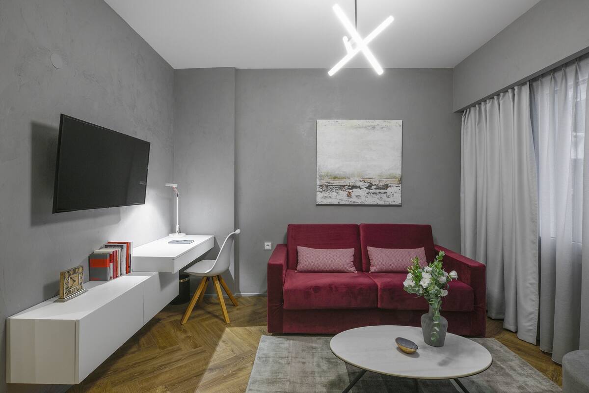 A modern living room with a flat-screen TV, a red sofa, a white desk, and a painting on the wall.