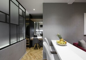 Una cocina moderna con comedor, que presenta una mesa blanca con frutero, una silla gris y un cojín rojo.