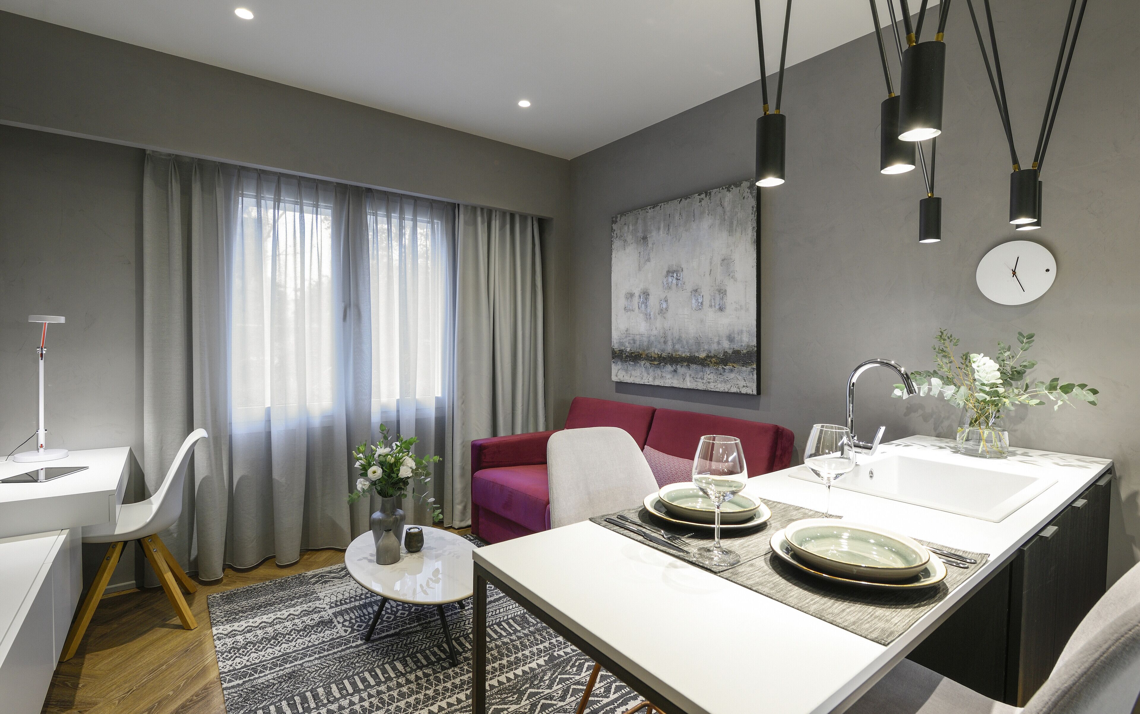 Ein modernes Wohnzimmer mit Essbereich, grauen Wänden, einem roten Sofa und einem großen abstrakten Gemälde.