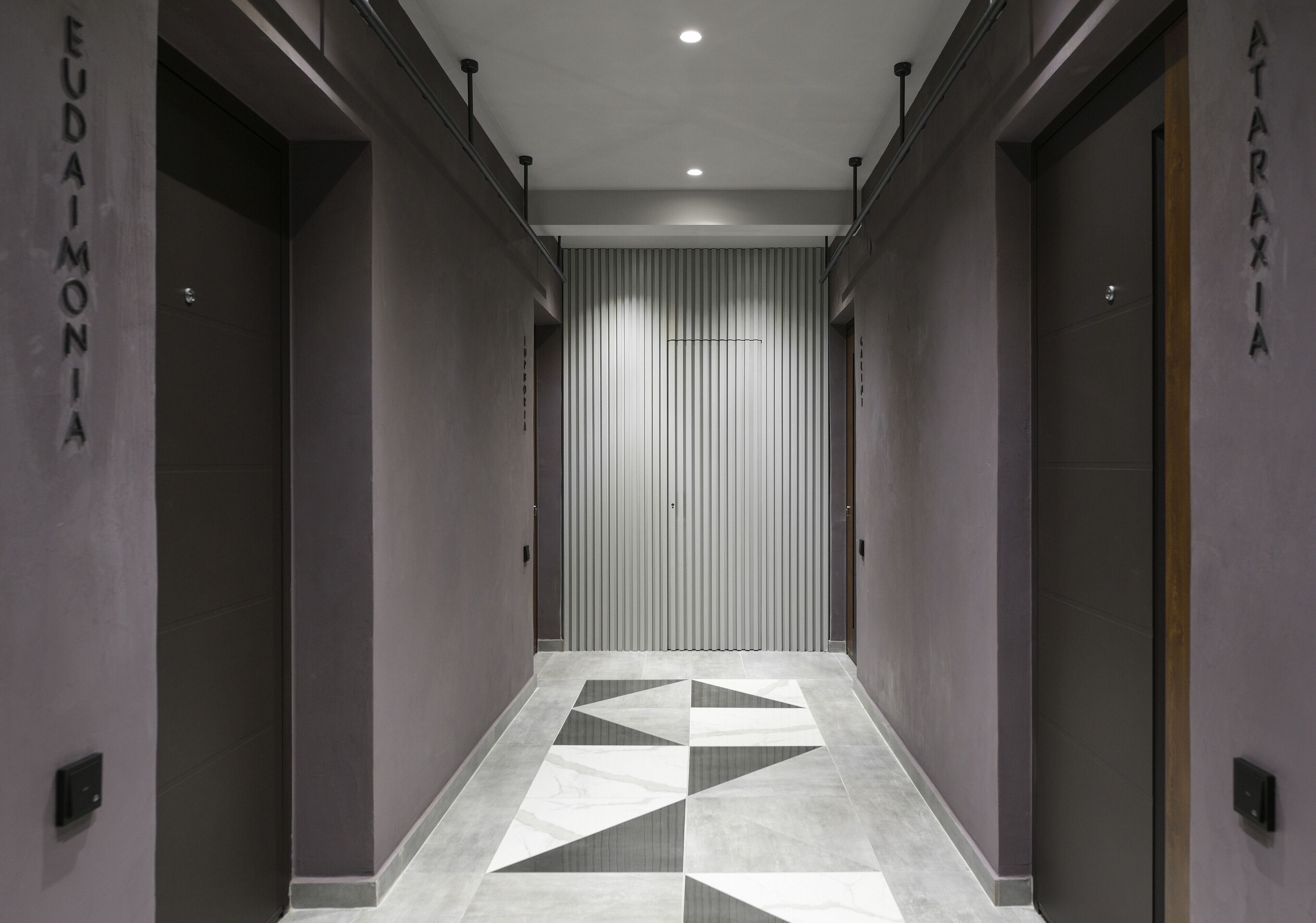 A modern hallway with a geometric patterned floor, flanked by doors labeled "EUDAINIA" and "ATARAXIA".