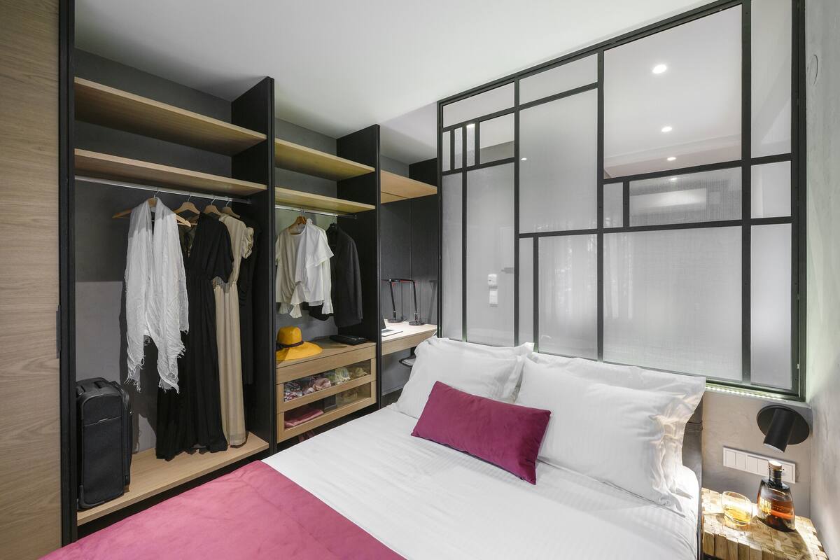 A modern hotel room with a bed, a wardrobe, a desk, and a large window.