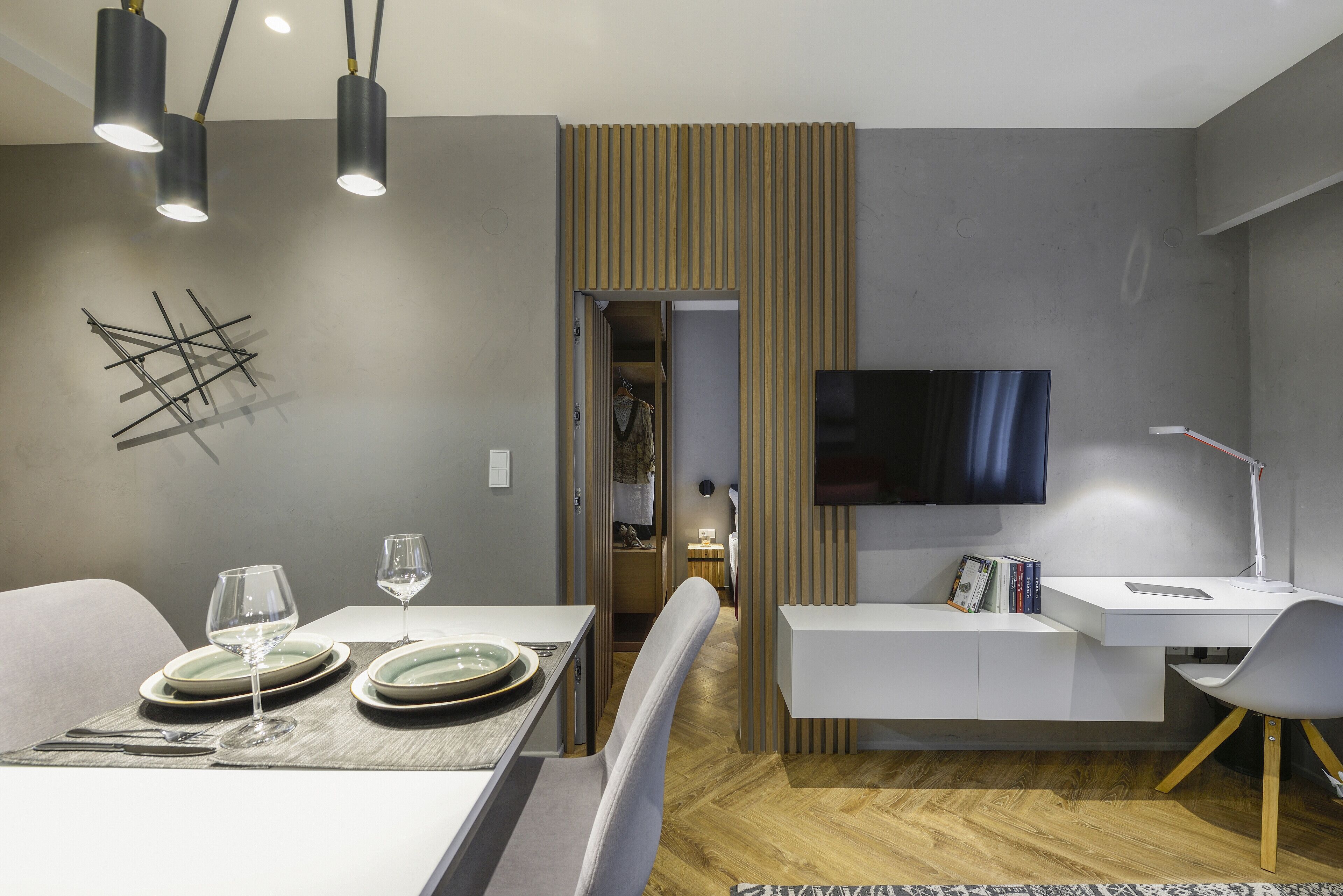 A modern dining area with a table set for two, a television mounted on the wall, and a desk with a chair.