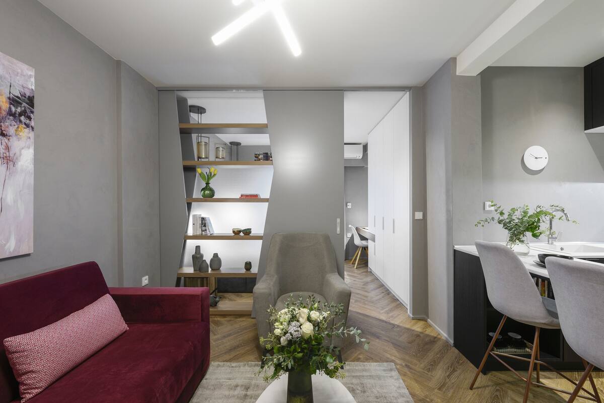 A modern living room with a red sofa, a grey armchair, and a dining area with a white table and grey chairs.