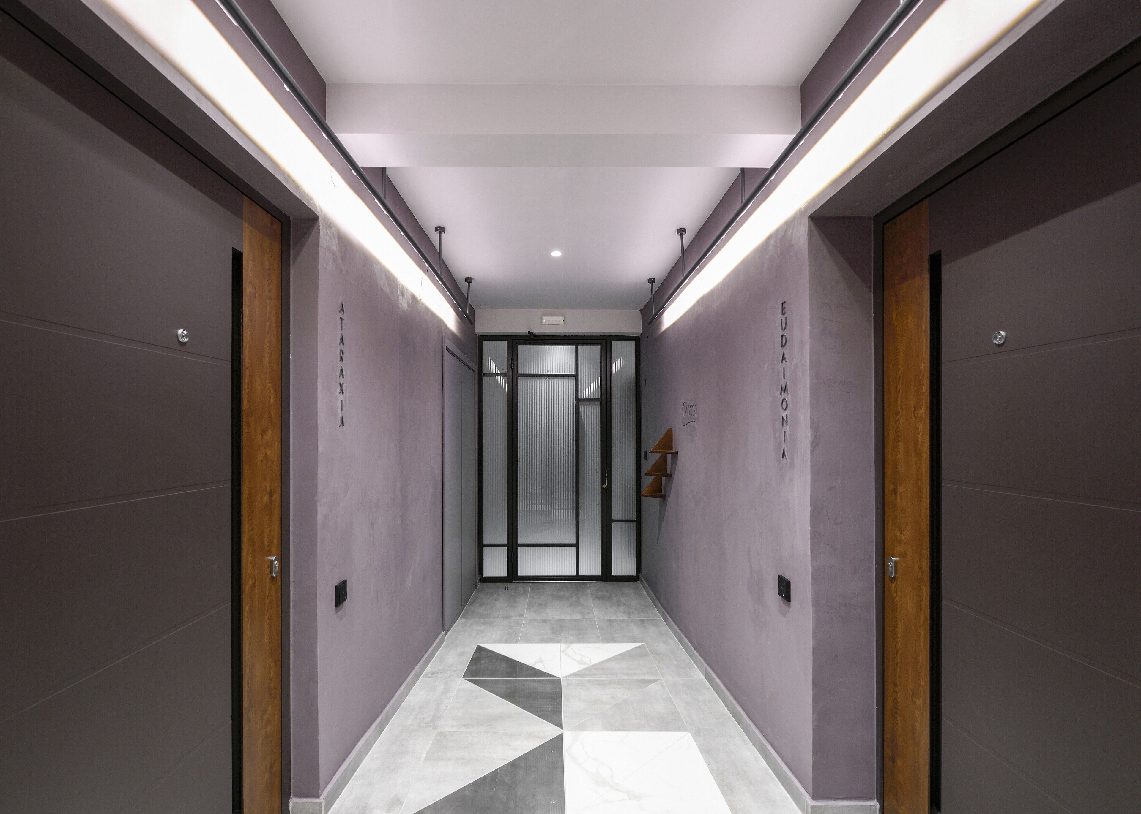 Un couloir moderne avec un sol à motifs géométriques, des murs gris et des portes en bois.
