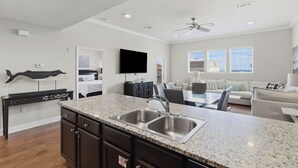 Una cocina moderna con encimeras de granito, lavamanos de acero inoxidable y una zona de comedor con una mesa de vidrio.