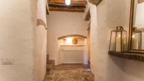 Un couloir étroit au sol dallé de pierre, aux murs blancs, au plafond en bois et à l’extrémité duquel se trouve une arche en pierre menant à une pièce.