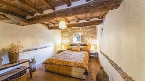 Une chambre à coucher rustique avec des poutres apparentes, un mur en pierre, un grand lit et un luminaire suspendu.