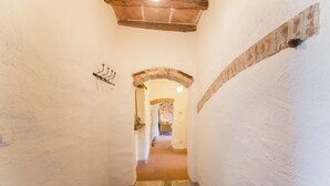 Un couloir étroit aux murs blancs, doté d’un sol en pierre et d’une arche en briques menant à une autre pièce.
