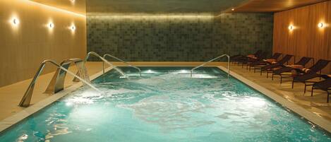A swimming pool with water jets, lounge chairs, and a tiled wall.