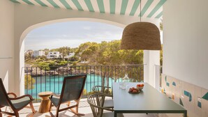 Un balcon avec vue sur une mer turquoise, une table avec des chaises et un luminaire suspendu.