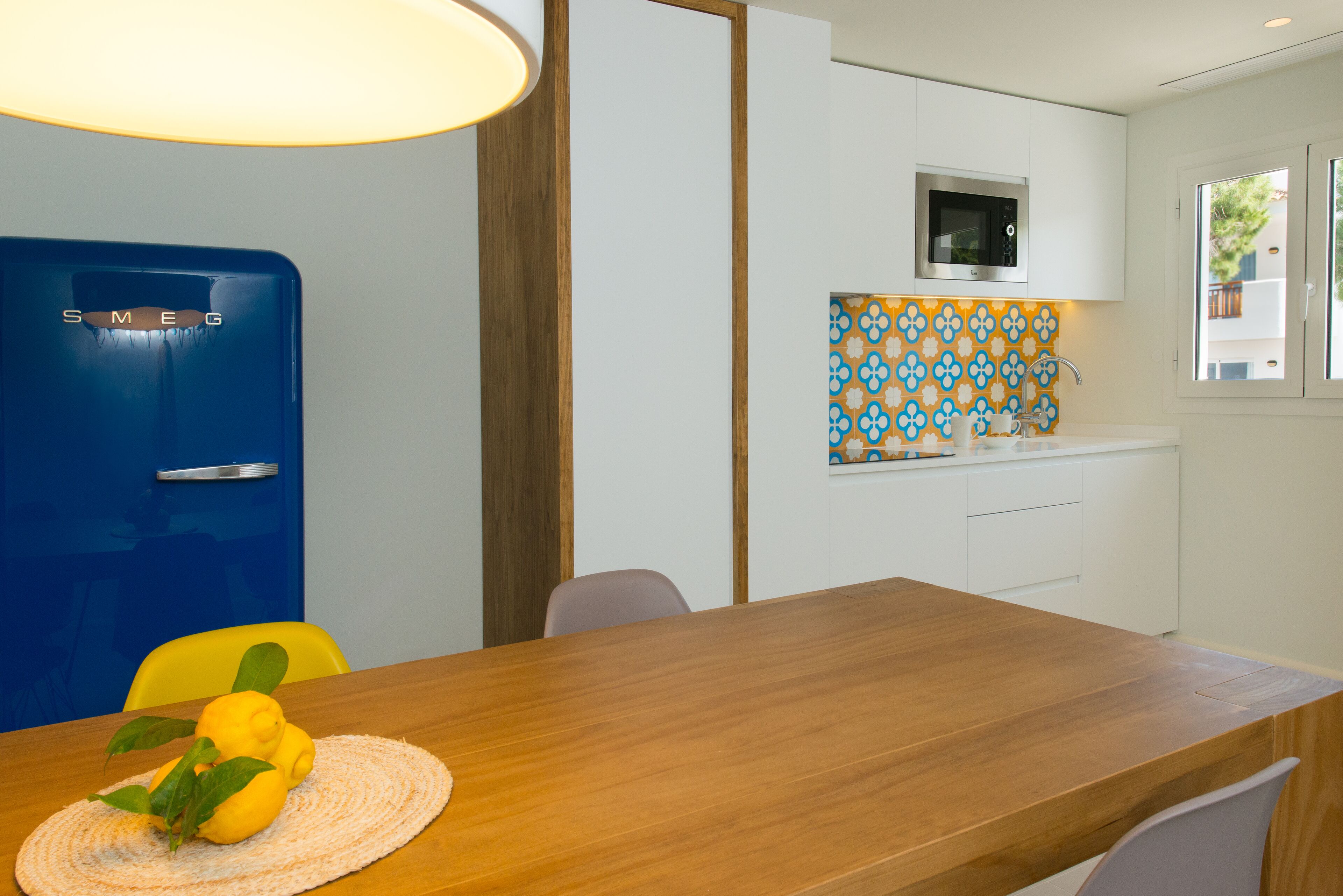 A modern kitchen with a blue refrigerator, a microwave, and a patterned backsplash.