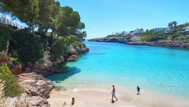 Un paysage côtier avec une eau turquoise cristalline, des falaises rocheuses et une plage de sable.