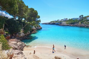 A coastal scene with clear turquoise water, rocky cliffs, and a sandy beach. - Inturotel Esmeralda Villas (Santanyi)