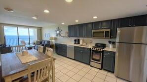 A modern kitchen with dark cabinets, stainless steel appliances, and a dining area with a view of the ocean. - BLDG Construction Aug-Oct 2026; See Desc below! Sea Winds 1203 (Marco Island)