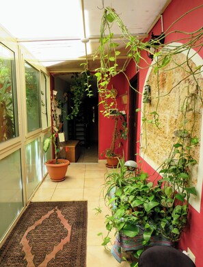 Un couloir étroit aux murs rouges, au sol carrelé, et où sont dispos ées diverses plantes en pot.