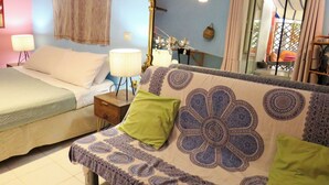 Quarto com cama, sofá, mesa de cabeceira, luminária e espelho.