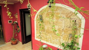 Quarto com parede vermelha, arco de pedra e diversos vasos de plantas.