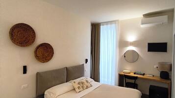 Habitació d'hotel amb un llit, una taula de treball, una cadira, un mirall i un aire condicionat fixat a la paret.