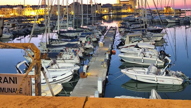Una marina con numerosos barcos amarrados, un muelle y un edificio con una torre al fondo.