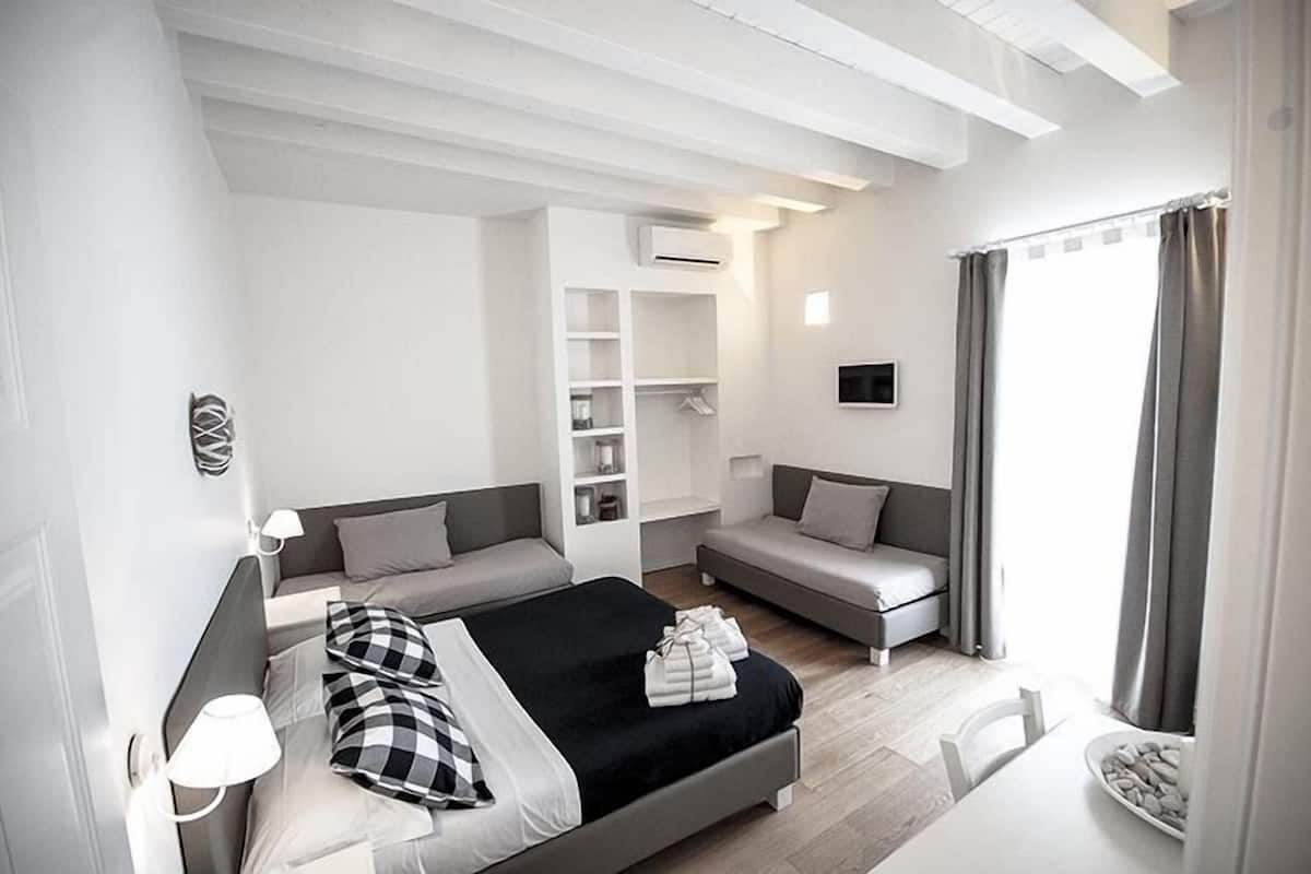 A modern hotel room with a bed, two sofas, a dining table, and a built-in wardrobe.