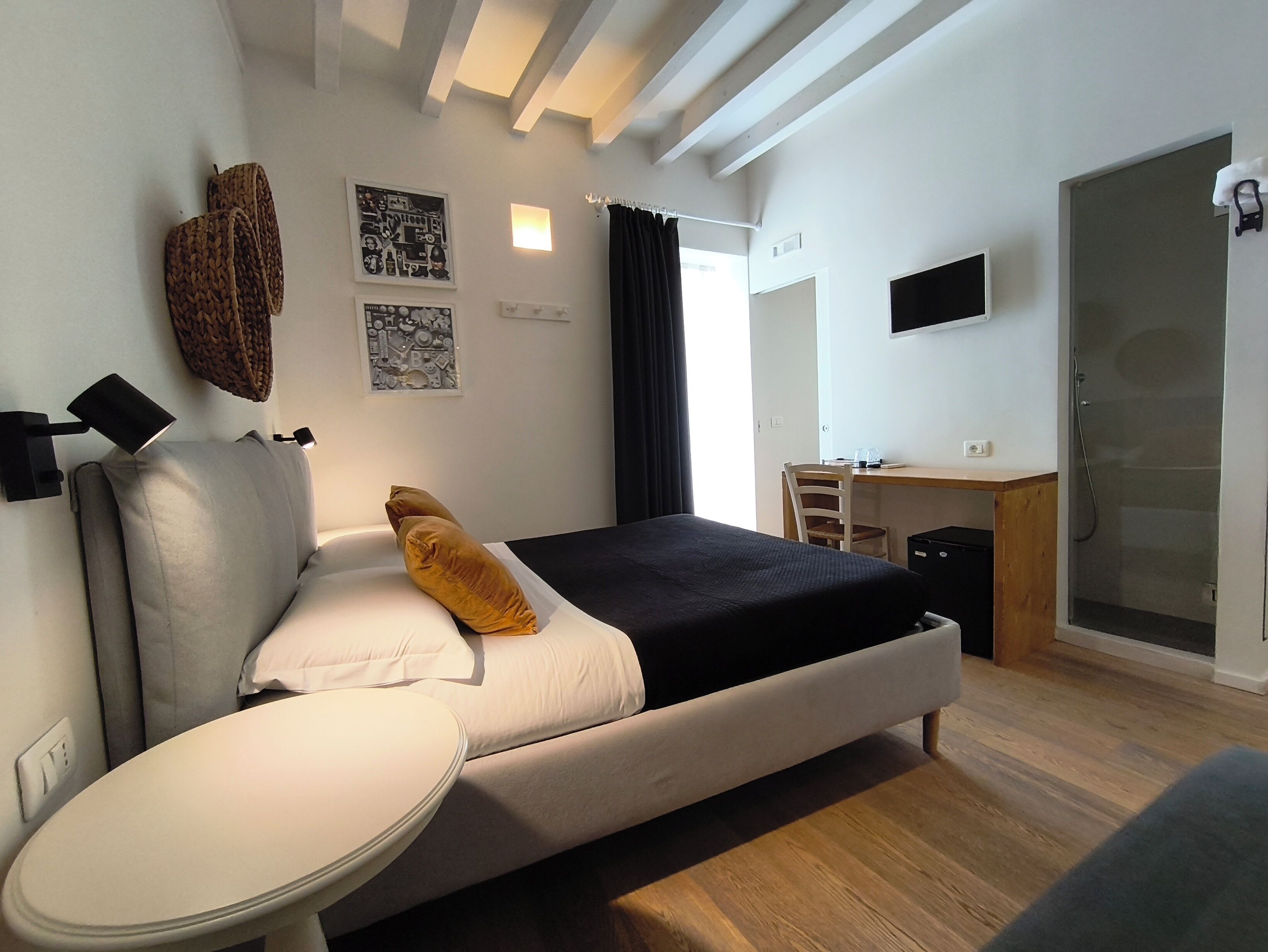 A modern hotel room with a bed, bedside table, desk, chair, and a shower area.