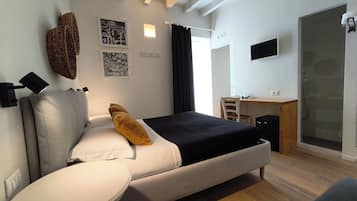 A modern hotel room with a bed, bedside table, desk, chair, and a shower area.