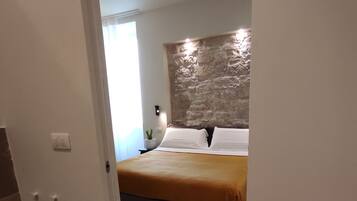 Ein Schlafzimmer mit einer Wand aus Stein, einem Bett mit weißen Leinen und einem kleinen Nachttisch mit einer Lampe.