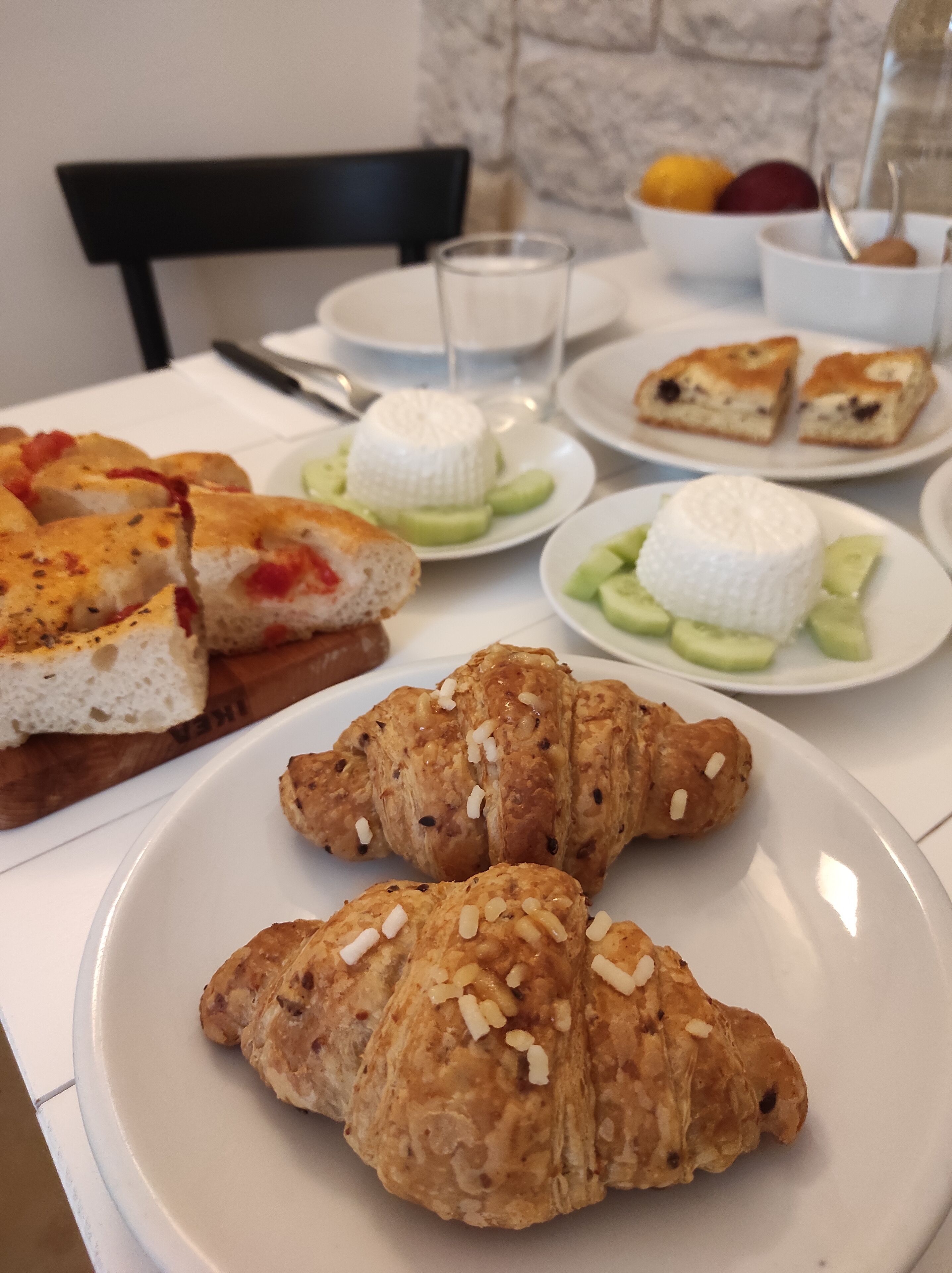 A table with various food items including croissants, a cheese wheel, and fruit.