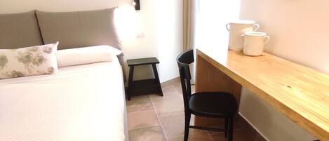 A bedroom with a bed, a desk, a chair, and a mirror.