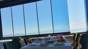 Une table dressée avec différents plats et boissons, offrant une vue panoramique sur la mer et les montagnes lointaines.