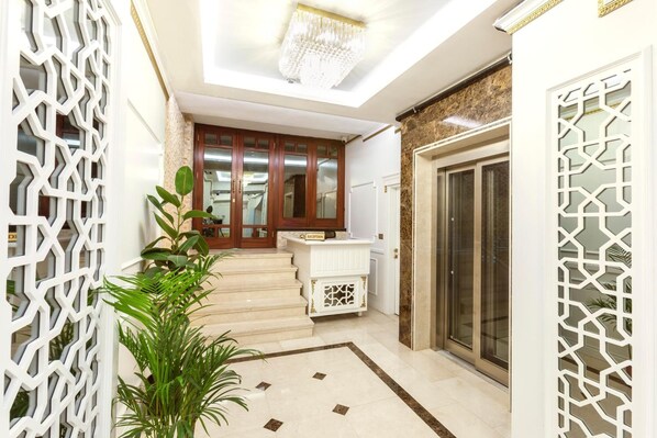 A modern hotel lobby with a reception desk, a staircase leading to the upper floor, and decorative screens.