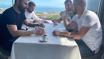 A group of people sitting at a table with a view of the sea and buildings in the background.