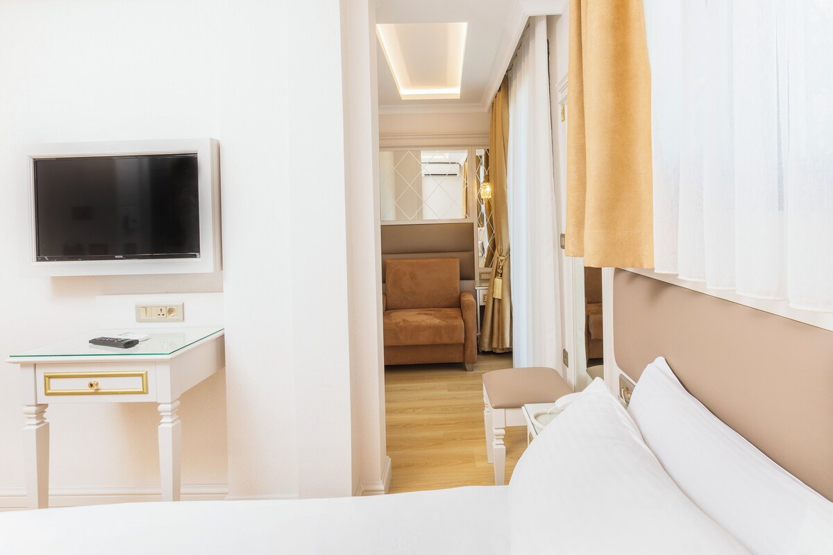 A hotel room with a bed, a TV, a desk with a remote, and a chair.