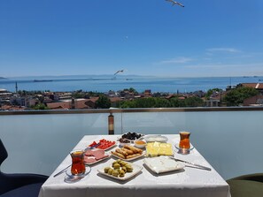 A table with food and drinks on a balcony overlooking a city and sea. - City Hall Hotel (Istanbul)