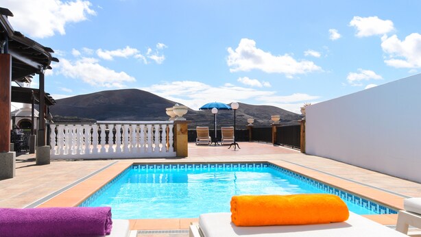 Une piscine avec des chaises longues et des serviettes, une clôture blanche et une montagne en arrière-plan.